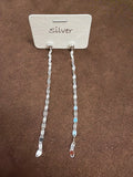 Pair of silver-tone long earrings with small round tops and a chain of flat oval elements, displayed on a white card marked Silver.