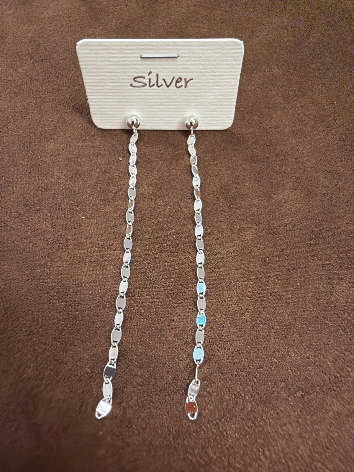 Pair of silver-tone long earrings with small round tops and a chain of flat oval elements, displayed on a white card marked Silver.