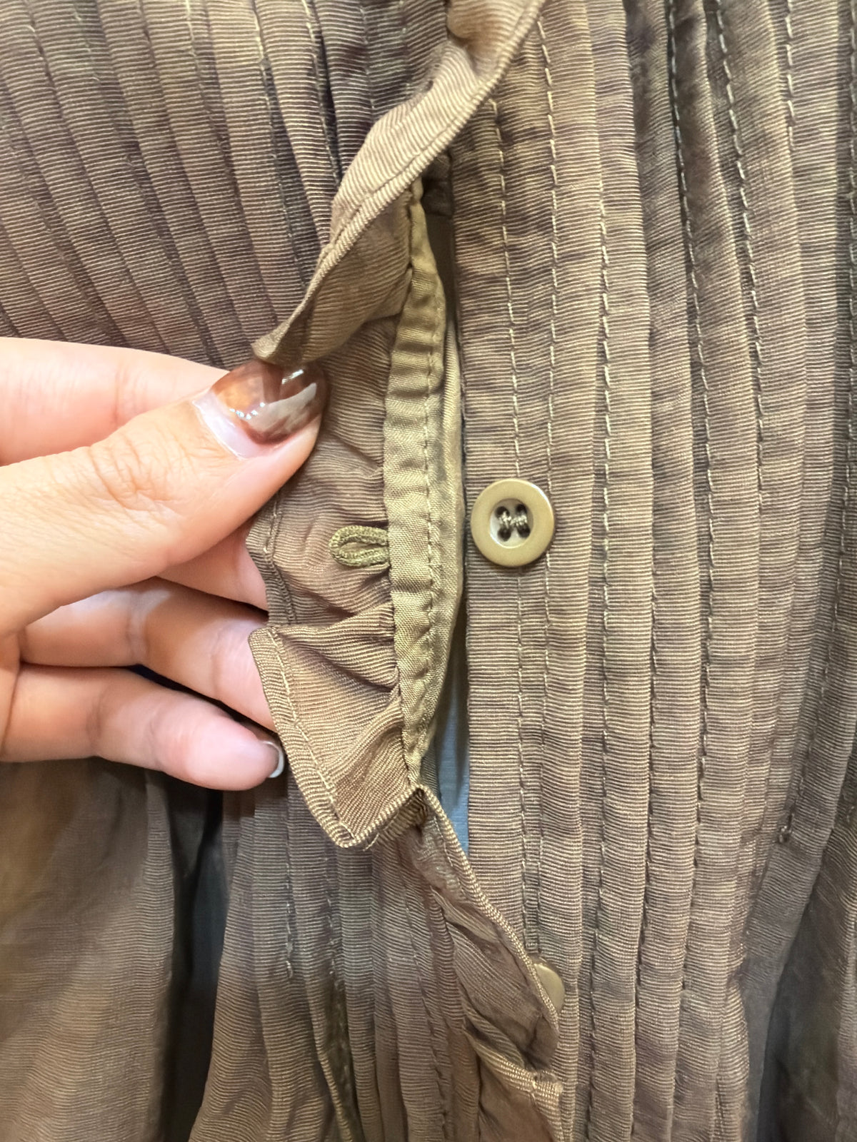 Close-up of H48 blouse front, showing vertical pintucks and a button-and-loop fastening beneath the ruffle trim.