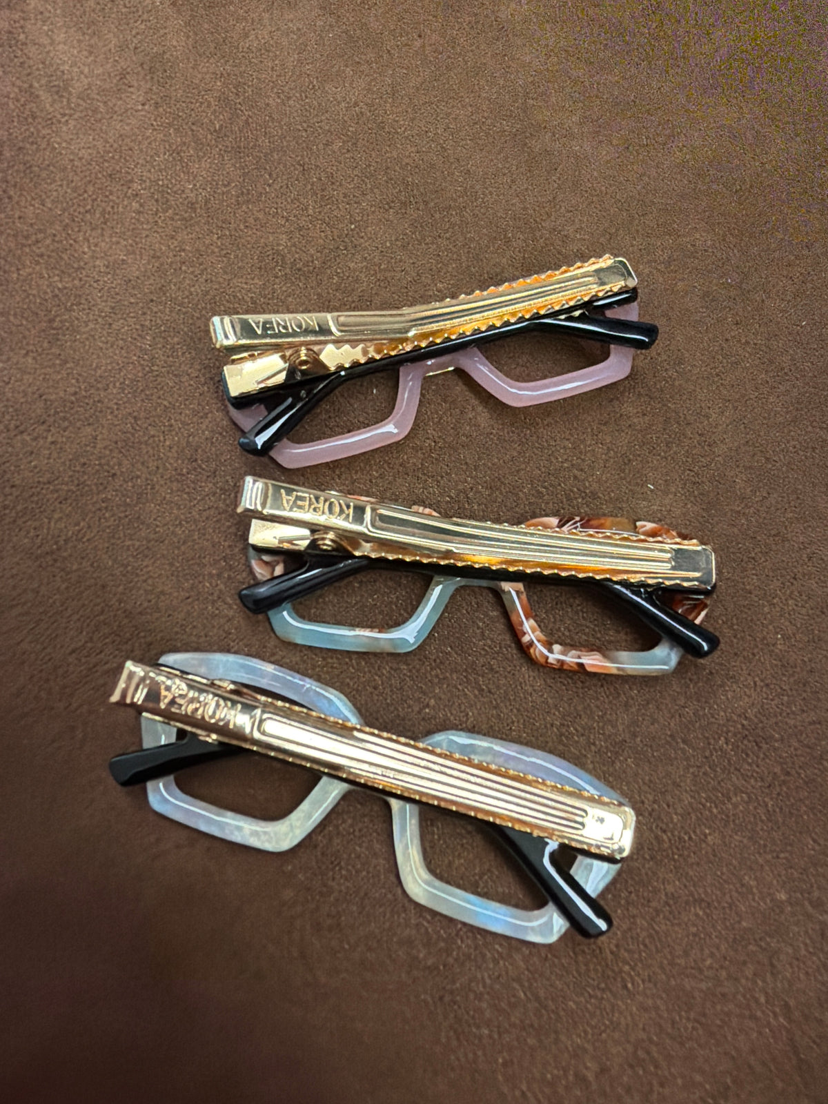 Reverse view of three glasses-shaped hair clips showing long gold-tone toothed clips and black glasses-arm details.