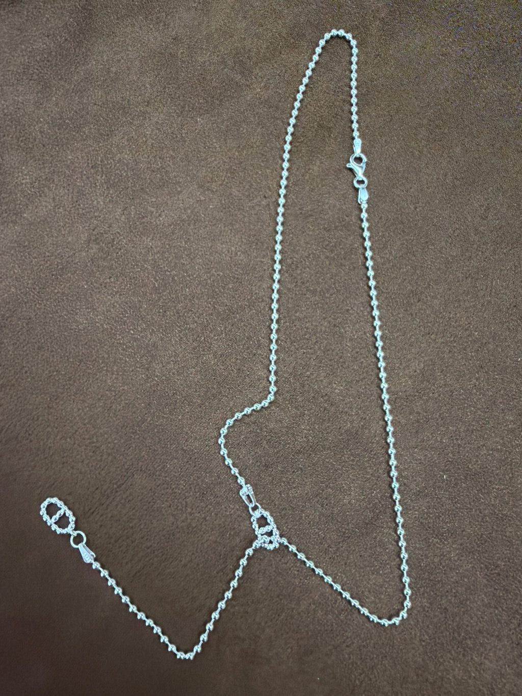 Silver-tone fine-chain necklace with textured open-link motifs and a trailing chain section, arranged on brown fabric.