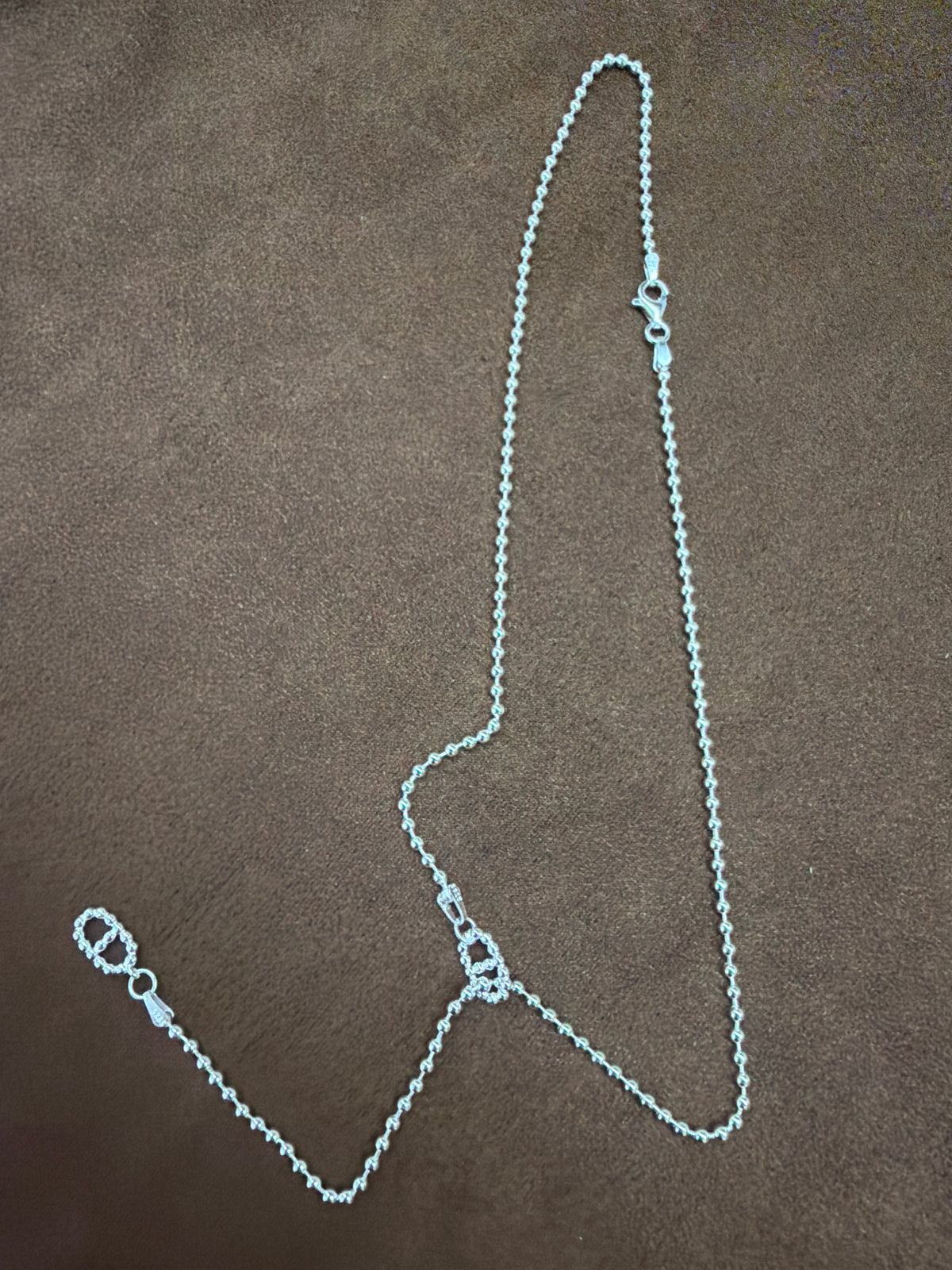 Silver-tone fine-chain necklace with textured open-link motifs and a trailing chain section, arranged on brown fabric.