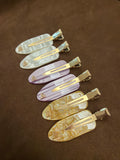 Six elongated hair clips with gold-tone clasps, showing ivory mosaic-like, pink striped and golden mosaic-like pearlescent-effect designs.