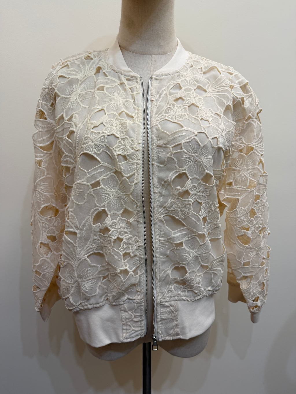 H44 ivory floral openwork lace jacket on a mannequin, with a front zip, long sleeves and plain neckline, cuff and hem trims.