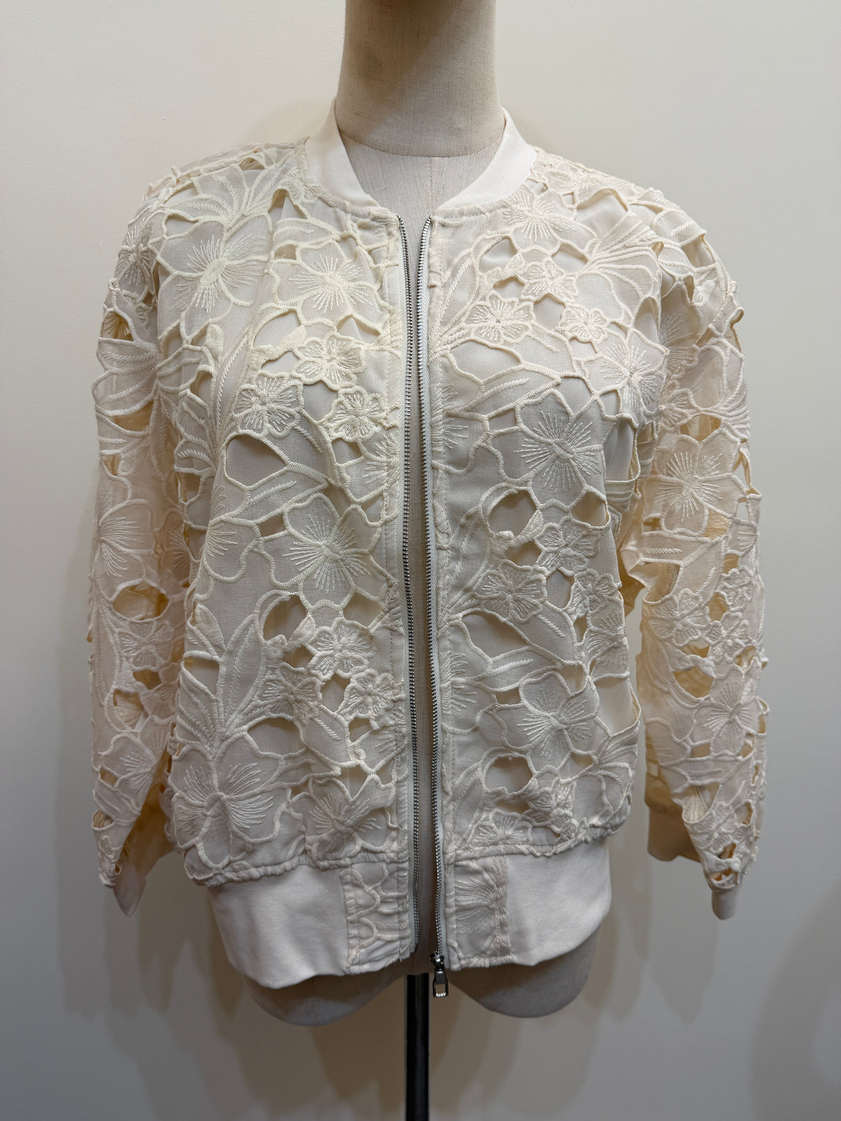 H44 ivory floral openwork lace jacket on a mannequin, with a front zip, long sleeves and plain neckline, cuff and hem trims.