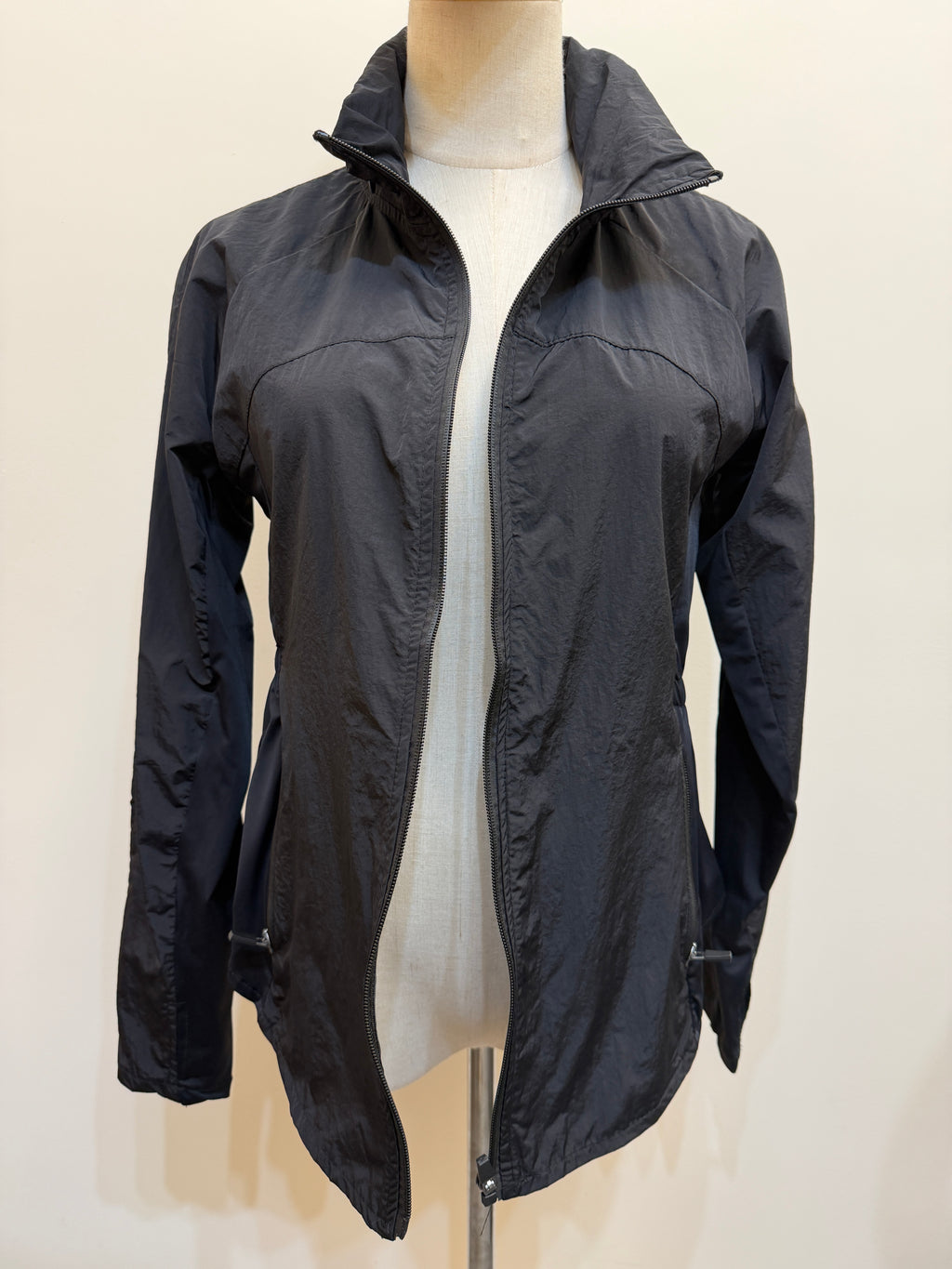 Front view of the H67 black jacket with the zip open, showing a stand collar, long sleeves, panelled design and front zip pockets.