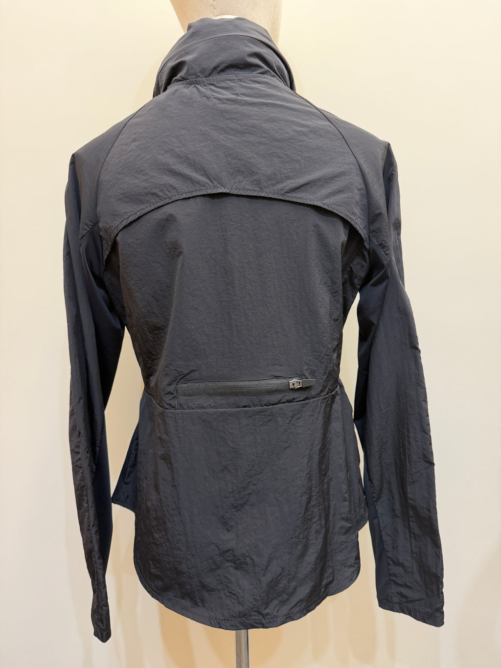 Back view of the H67 black jacket, showing a curved upper-back overlay, long sleeves and a horizontal lower-back zip pocket.