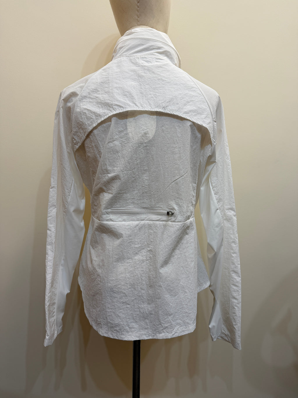 Back view of the H67 white jacket, showing a curved upper-back overlay, sleeve panels and a horizontal zip pocket at the lower back.