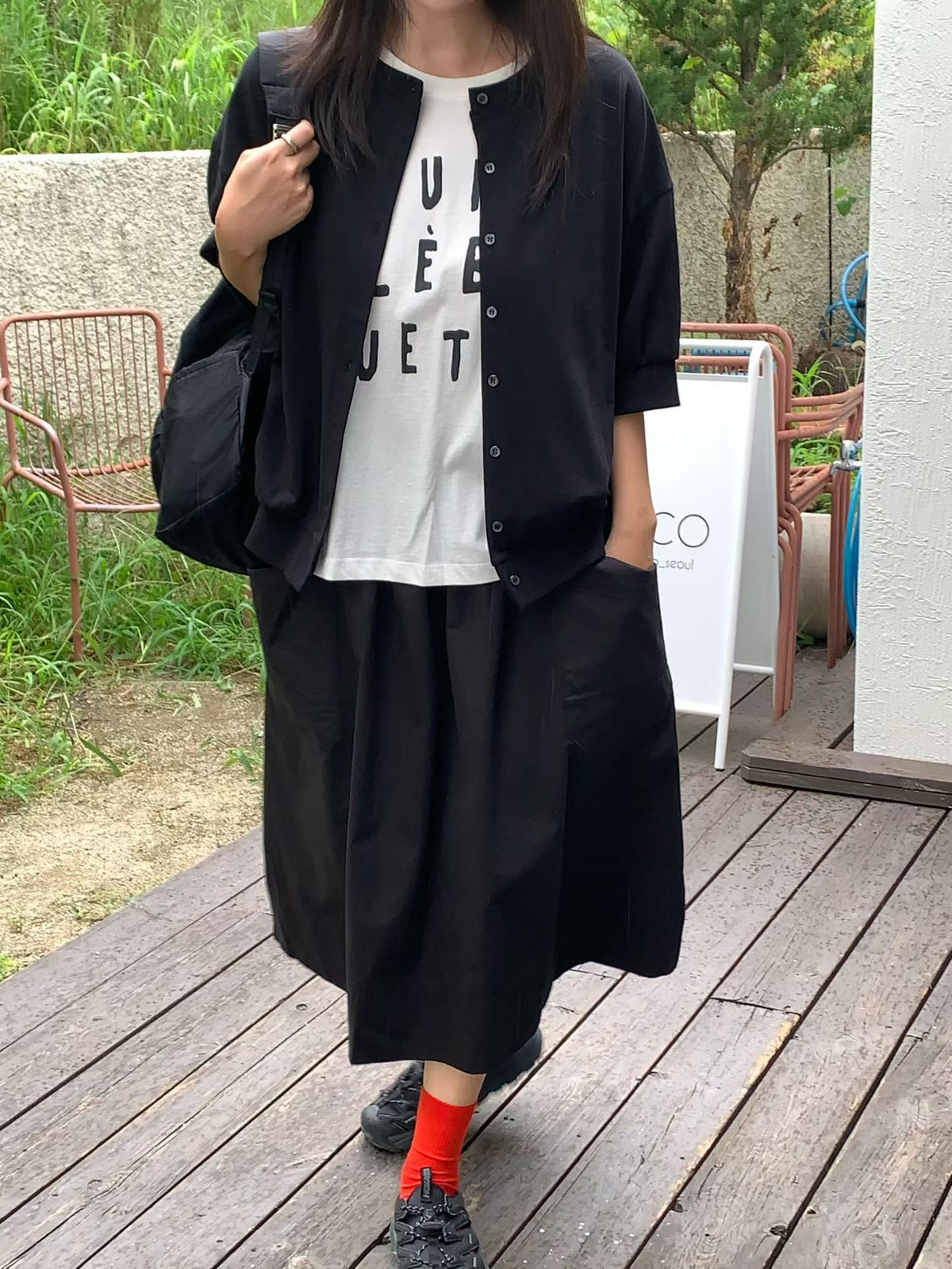 H62 black half-sleeve button-front jacket worn open over a white graphic T-shirt with a black skirt, photographed outdoors.