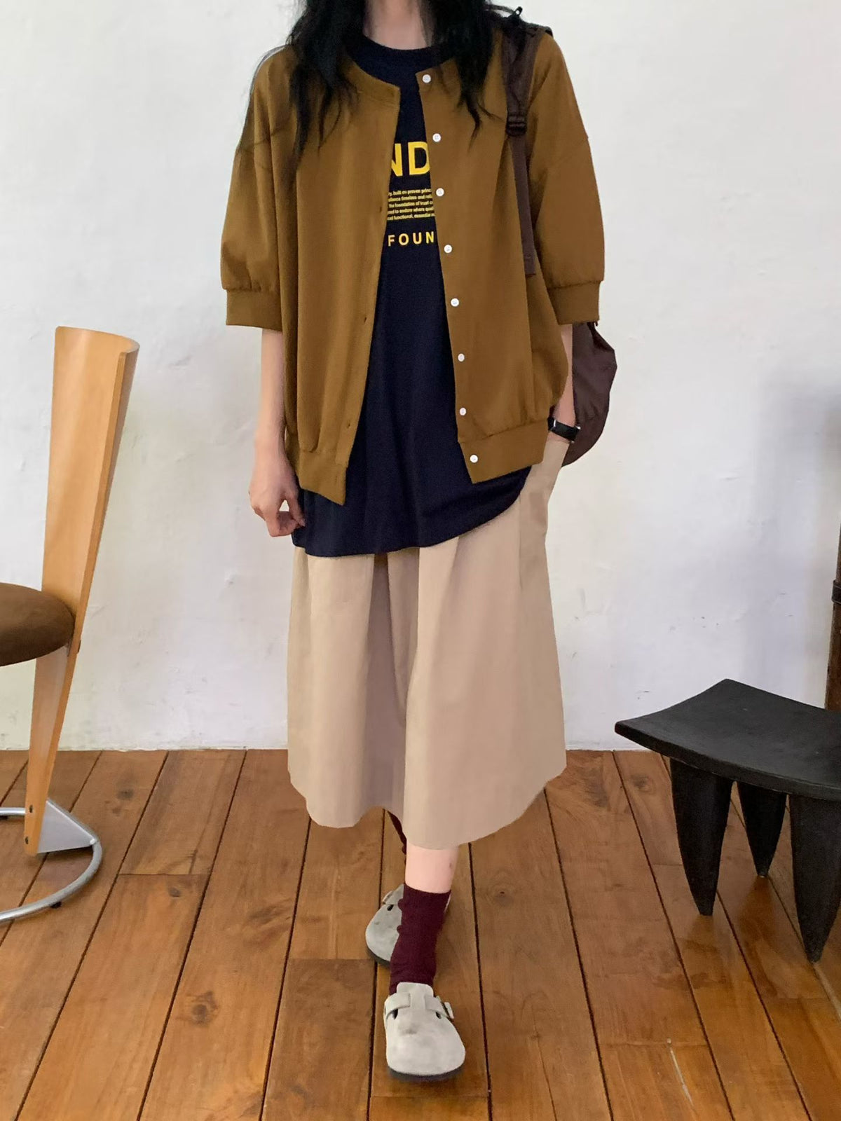 H62 brown round-neck jacket worn open over a navy graphic T-shirt with beige wide-leg bottoms, showing dropped shoulders and banded cuffs.