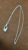 A62 silver necklace with an irregular textured open pendant, rectangular bail and fine rope-like chain on brown fabric.