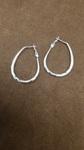Pair of silver teardrop-shaped hoop earrings with small reflective surface markings and upper post clasps on brown fabric.