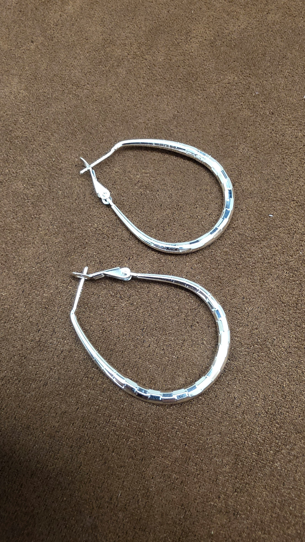 Angled view of silver teardrop hoop earrings showing the facet-like surface details and hinged clasp structures.